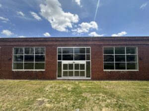 Brick storefront on a sunny, blue sky day showing the newly installed windows and door leading into the future grocery store.