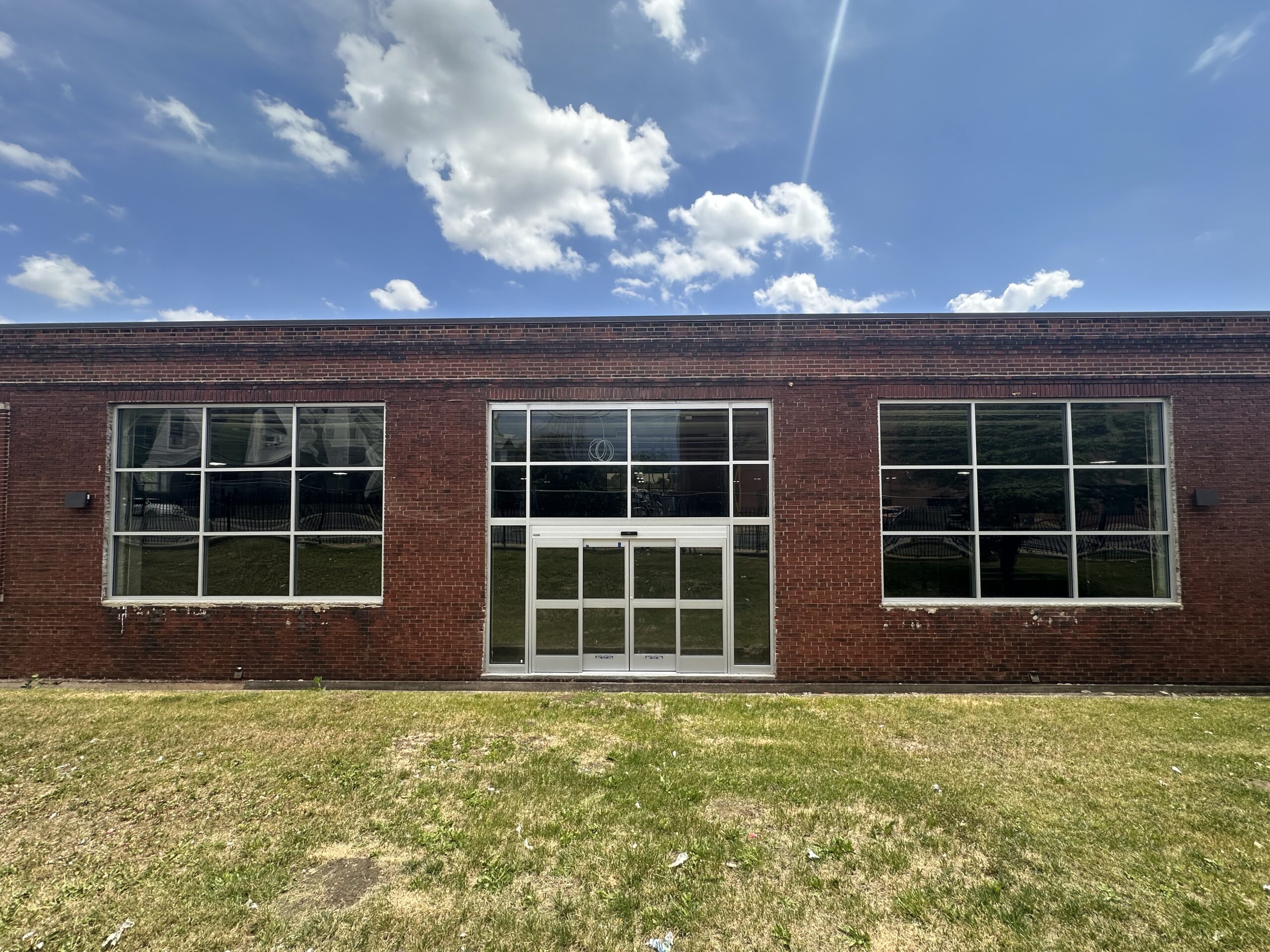 Brick storefront on a sunny, blue sky day showing the newly installed windows and door leading into the future grocery store.