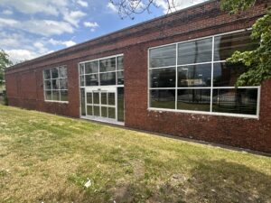 Brick storefront on a sunny, blue sky day showing the newly installed windows and door leading into the future grocery store.